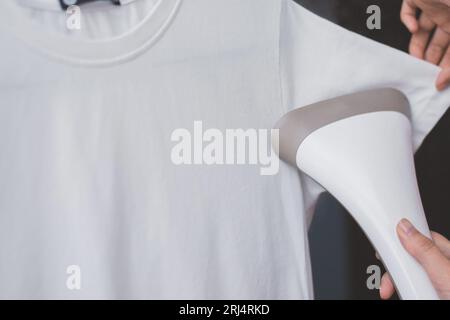 Nahaufnahme auf einem Dampfer in der Hand einer Frau, die ein weißes T-Shirt dampfte, Kopierraum Stockfoto