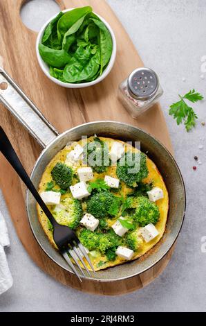 Omelette mit Brokkoli und Feta-Käse in einer Pfanne, gebackenes Omelett auf hellem Hintergrund Stockfoto