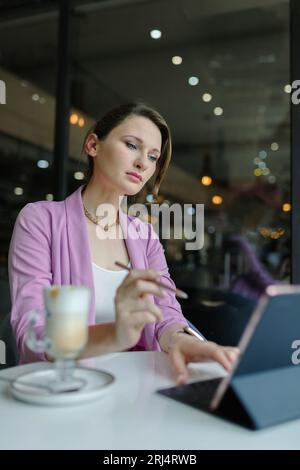Stift von einem Tablet in der Hand einer Frau vor einem Tablet auf einem Tisch im Café, Kopierraum, vertikal Stockfoto