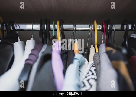 Verschiedene Kleidungsstücke hängen zufällig auf verschiedenen Kleiderbügeln, Nahaufnahme Stockfoto