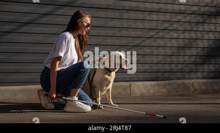 Eine blinde Frau geht mit ihrem Blindenhund auf die Straße. Ein Mädchen, das einen labrador umarmt. Stockfoto