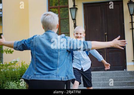 Mutter trifft Kinder aus der Schule. Kaukasischer Junge und Mädchen laufen auf ihre Mutter zu und umarmen sie. „Back to School“-Konzept Stockfoto