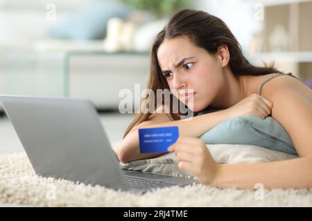 Verwirrte Frau, die zu Hause mit Laptop und Kreditkarte online kauft Stockfoto