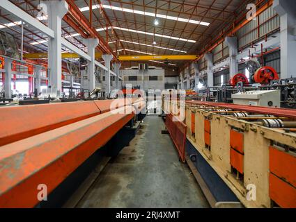 Eine robuste Industriemaschine, die in den Fertigungsprozess eingebunden ist. Großer Kran und Förderband befinden sich im Arbeitsbereich. Stockfoto