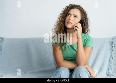 Schöne junge Erwachsene Frau mit Telefon wartet drinnen auf Hilfe zu Hause Stockfoto