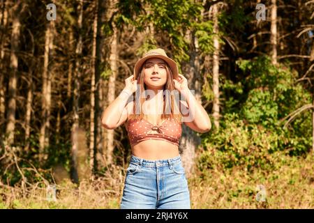 Eine kaukasische Frau in einer Crop Top posiert in einem üppigen grünen Wald zur goldenen Stunde Stockfoto