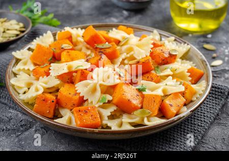 Pasta mit geröstetem Kürbis, Farfalle Pasta mit Kürbis auf einem Teller auf dunklem rustikalem Hintergrund Stockfoto