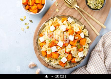 Pasta mit geröstetem Kürbis, Farfalle Pasta mit Kürbis und Feta-Käse auf einem Teller auf hellem Hintergrund Stockfoto