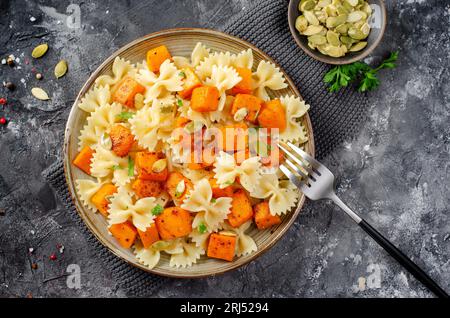 Pasta mit geröstetem Kürbis, Farfalle Pasta mit Kürbis auf einem Teller auf dunklem rustikalem Hintergrund Stockfoto