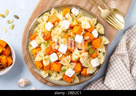 Pasta mit geröstetem Kürbis, Farfalle Pasta mit Kürbis und Feta-Käse auf einem Teller auf hellem Hintergrund Stockfoto