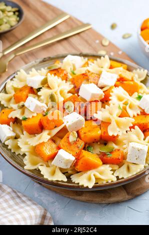 Pasta mit geröstetem Kürbis, Farfalle Pasta mit Kürbis und Feta-Käse auf einem Teller auf hellem Hintergrund Stockfoto