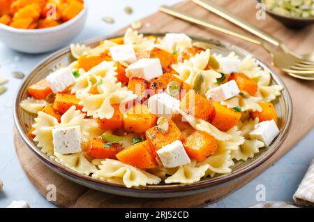 Pasta mit geröstetem Kürbis, Farfalle Pasta mit Kürbis und Feta-Käse auf einem Teller auf hellem Hintergrund Stockfoto