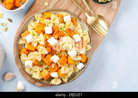 Pasta mit geröstetem Kürbis, Farfalle Pasta mit Kürbis und Feta-Käse auf einem Teller auf hellem Hintergrund Stockfoto