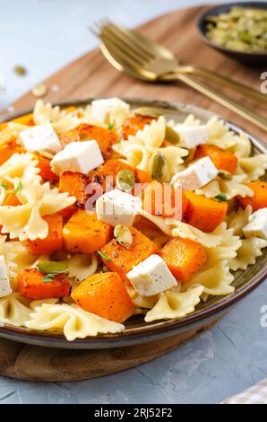 Pasta mit geröstetem Kürbis, Farfalle Pasta mit Kürbis und Feta-Käse auf einem Teller auf hellem Hintergrund Stockfoto