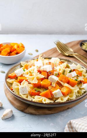 Pasta mit geröstetem Kürbis, Farfalle Pasta mit Kürbis und Feta-Käse auf einem Teller auf hellem Hintergrund Stockfoto
