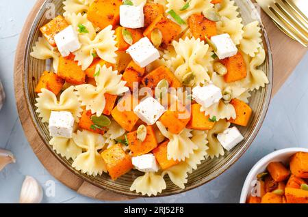 Pasta mit geröstetem Kürbis, Farfalle Pasta mit Kürbis und Feta-Käse auf einem Teller auf hellem Hintergrund Stockfoto