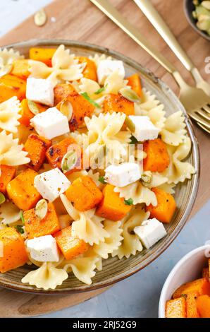 Pasta mit geröstetem Kürbis, Farfalle Pasta mit Kürbis und Feta-Käse auf einem Teller auf hellem Hintergrund Stockfoto