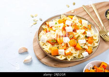 Pasta mit geröstetem Kürbis, Farfalle Pasta mit Kürbis und Feta-Käse auf einem Teller auf hellem Hintergrund Stockfoto