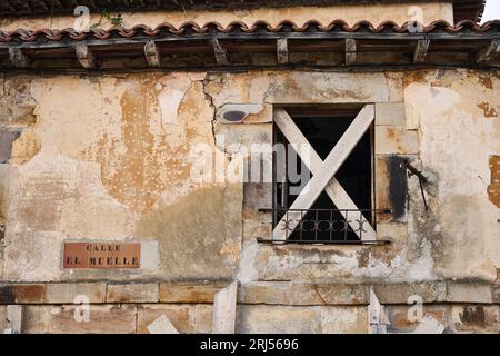 Nahansicht der Steinfassade mit Holzfenster, das mit zwei x-förmigen Holzlatten blockiert ist Stockfoto