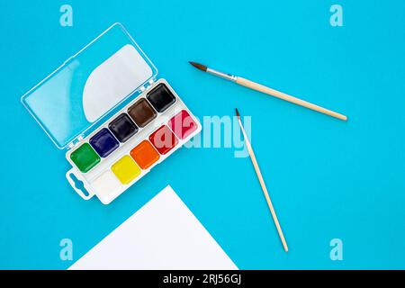 Aquarelle und Pinsel auf blauem Hintergrund, flache Anordnung, Draufsicht. Stockfoto