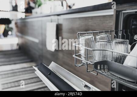Schließung der geöffneten automatischen, eingebauten Geschirrspülmaschine aus rostfreiem Edelstahl in der modernen Hausküche mit sauberem Utensilien. Hausarbeit, täglich zu Hause Stockfoto
