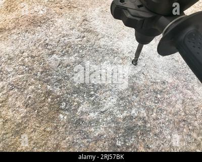 Ein robuster Hartmetallbohrer bohrt ein Loch in einen großen grauen Stein. Ansicht schließen. Der Hintergrund. Stockfoto