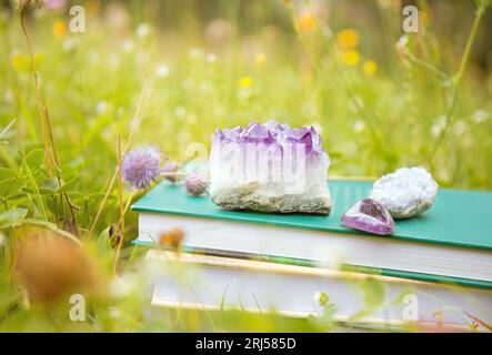 Selbsthilfe oder esoterische Themenbücher im Stapel mit Kristallgeoden im Freien an sonnigen Sommertagen mit blokeh Natur Wiesengarten im Hintergrund. Stockfoto