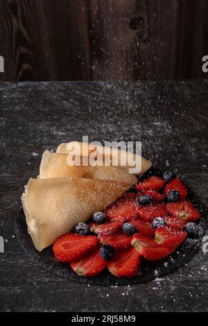 Foto von Reifen Erdbeeren und Blaubeeren und Pfannkuchen und Puderzucker, die darauf bestreut sind. Stockfoto