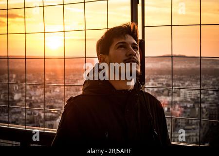 Ein junger Mann auf der Spitze des Eiffelturms, der in den Himmel blickt Stockfoto
