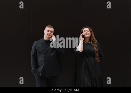 Junge Liebende, Frauen und Männer in schwarzen Kleidern, hören Audiobotschaften Stockfoto