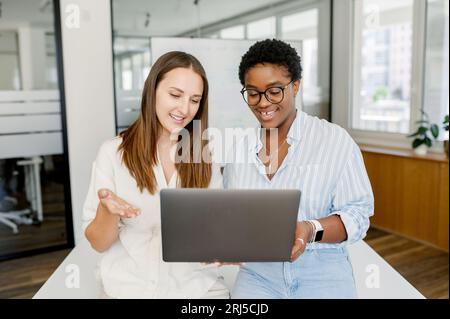 Gute Zusammenarbeit und freundliche Büroatmosphäre. Zwei weibliche Kollegen, die über das Projekt auf dem Laptop diskutieren. Mentor oder Coach, der das Projekt der Praktikantin durchschaut, zwei Frauen mit Computer im Büro Stockfoto