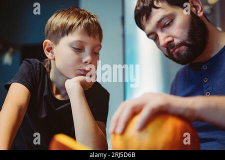 kaukasischer Mann mit Kind, der eine traditionelle Jack-Laterne aus Kürbis schnitzt. Halloween-Konzept. Bild mit selektivem Fokus Stockfoto