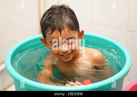 Ein fröhlicher südasiatischer Junge, der in einer mit Wasser gefüllten Badewanne im Badezimmer spielt Stockfoto