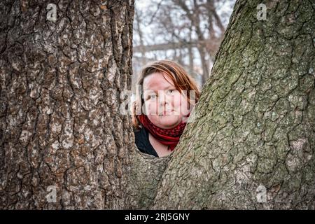 Porträt eines lächelnden Mädchens, das sich hinter einem Baumstamm versteckt Stockfoto