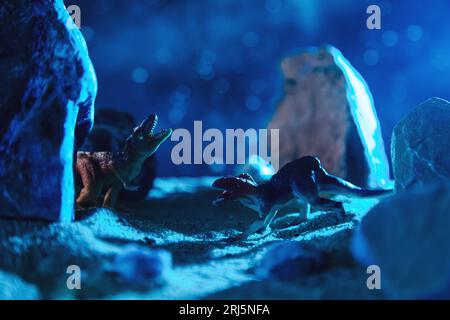 Zwei Dinosaurier kämpfen nachts in einer Felsschlucht. Kreative Landschaft mit einer kleinen Miniatur. Stockfoto