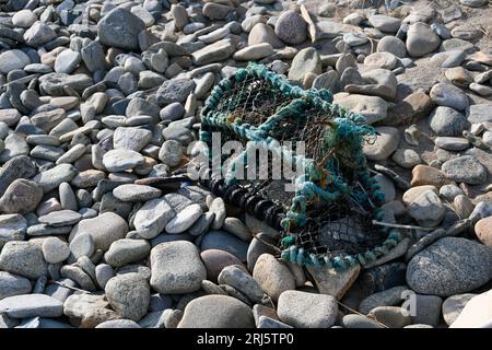 Eine alte Hummer-Falle, die an einem sonnigen Tag an einem steinigen Strand angespült wurde Stockfoto