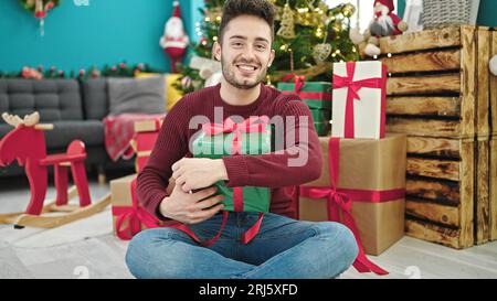 Junger lateinamerikanischer Mann mit einem weihnachtsgeschenk, der zu Hause lächelt Stockfoto