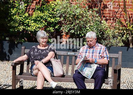 Roggen, East Sussex, Großbritannien. August 2023. Wetter in Großbritannien: Besucher der antiken Stadt Rye laufen entlang der Hauptstraße bei herrlichem Sonnenschein am Vormittag. Ein älteres Paar sitzt auf einer Bank im Sonnenschein, der Mann liest eine Kopie der Spiegelzeitung. Foto: PAL News/Alamy Live News Stockfoto