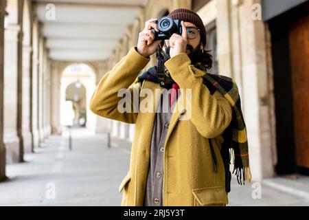 Ein Tourist, der ein Foto mit seiner Kamera in der Stadt macht. Männlicher Fotograf, der Spaß hat bei Winterurlauben auf der Straße Stockfoto