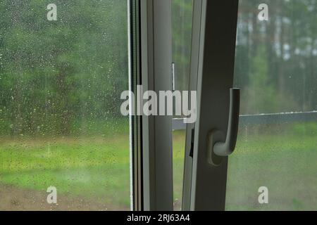 Regentropfen in einem Fensterbereich. Regentropfen auf transparentem Glas auf grünem Hintergrund. Weichzeichner. Das Konzept von Traurigkeit, schlechter Stimmung, nass. Grauer Himmel. Regnerischer Sommer Stockfoto