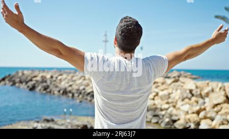 Junger lateinamerikanischer Mann, der mit offenen Armen am Strand steht und atmet Stockfoto