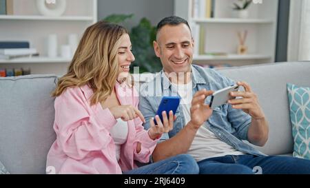 Mann und Frau, die zu Hause auf dem Sofa sitzen und Smartphones benutzen Stockfoto