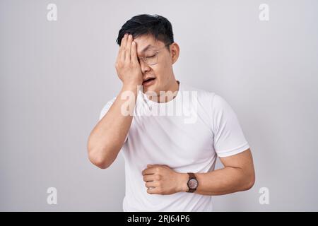 Junger asiatischer Mann, der auf weißem Hintergrund steht und müde ist, das halbe Gesicht, Auge und Mund mit der Hand bedeckt. Das Gesicht schmerzt vor Schmerzen. Stockfoto