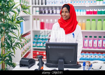 Junge schöne Frau Apotheker lächelt zuversichtlich mit Computer in der Apotheke Stockfoto