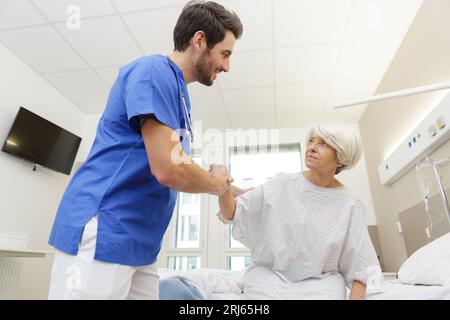 Pflegefachkraft hilft älteren Patienten vom Krankenhausbett Stockfoto