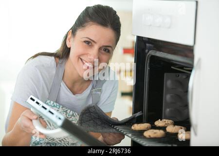 Frau nimmt Backblech mit Keksen aus dem Ofen Stockfoto