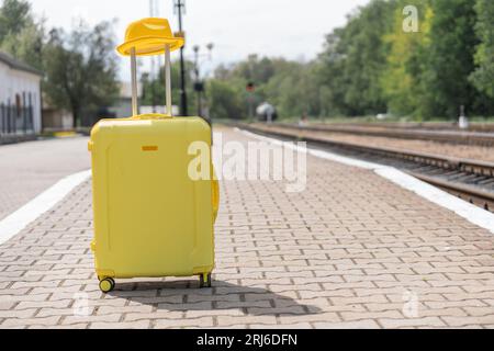 Ein gelber Koffer mit Hut steht auf einer Plattform. Gepäck vor dem Urlaub. Koffer für Reisen und Reisen im Urlaub. Stockfoto