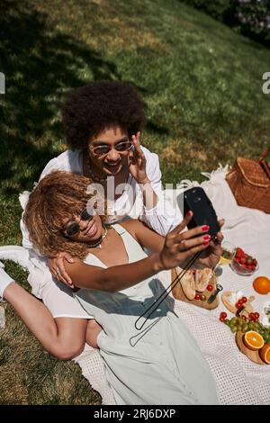 Top-Ansicht von überschwänglichen afroamerikanischen Freundinnen, die Selfie auf Vintage-Kamera machen, Sommer-Picknick Stockfoto