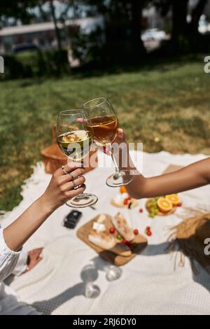 Abgeschnittene Ansicht von afroamerikanischen Frauen, die Weingläser klatschen, Essen auf verschwommenem Hintergrund, Picknick Stockfoto