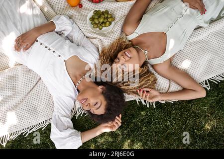 Sommerpicknick, afroamerikanische Freundinnen entspannen auf Decke, Obst, geschlossene Augen, Blick von oben Stockfoto